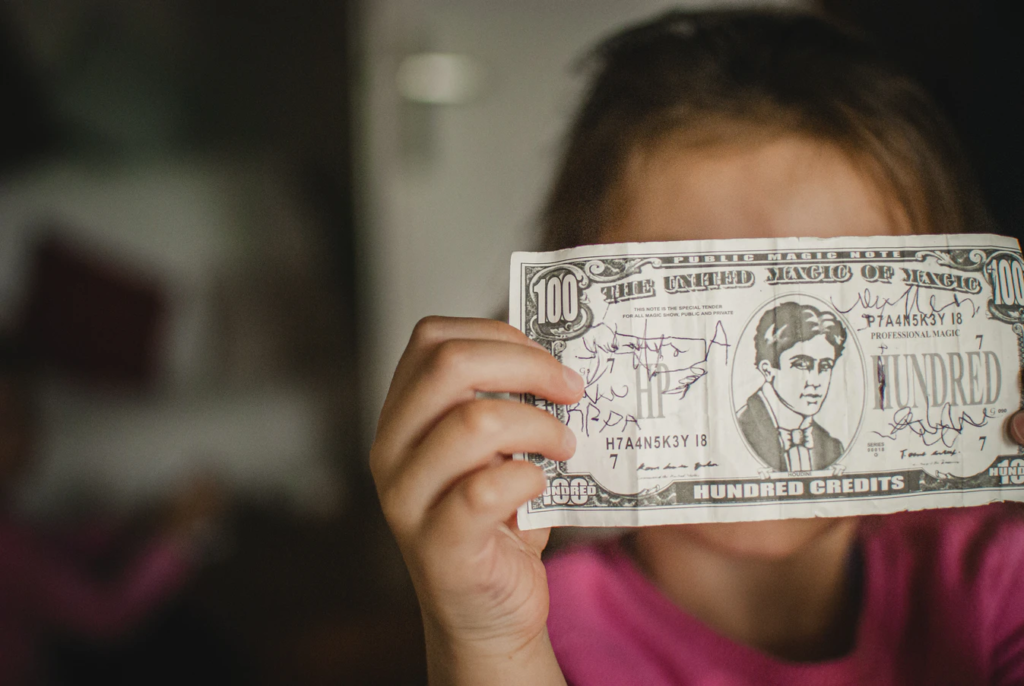Why Don't Pro-Life Advocates Support Policies to Reduce Unwanted Pregnancies? A child holding a novelty banknote labeled "The United Mago of Magic" and "Hundred Credits" in front of their face.
